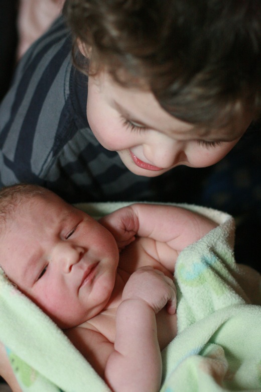 big brother and baby brother meeting — older sibling peering into newborn's face