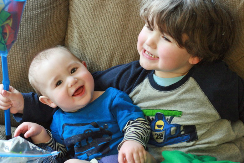 brothers sitting next to each other on the couch — siblings smiling — baby Alrik a8mo mikko m4yo