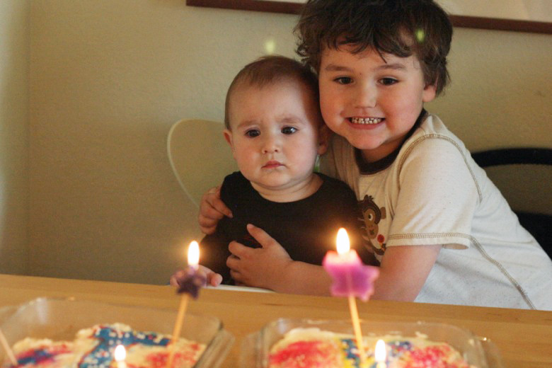 boy and baby with first birthday cake and lit candles