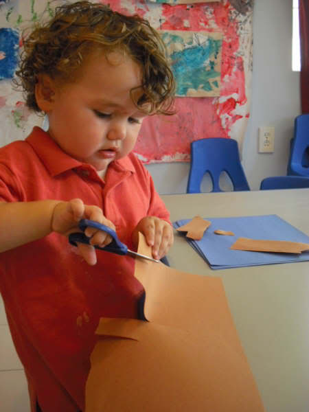 toddler cutting construction paper artwork with scissors