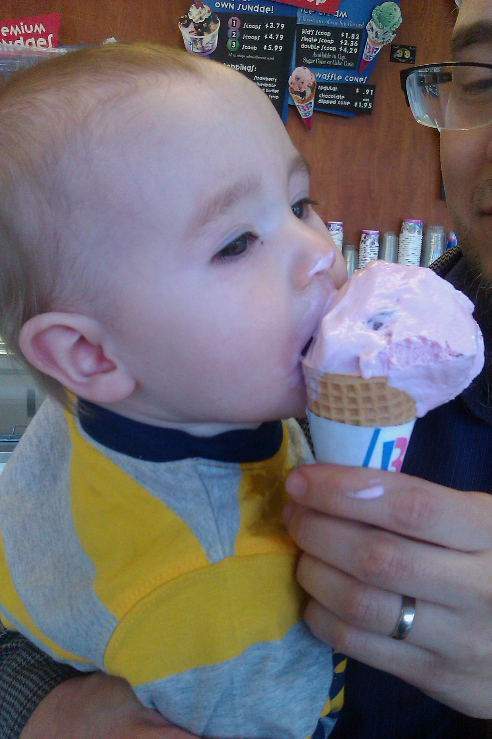 baby eating ice cream cone held by father