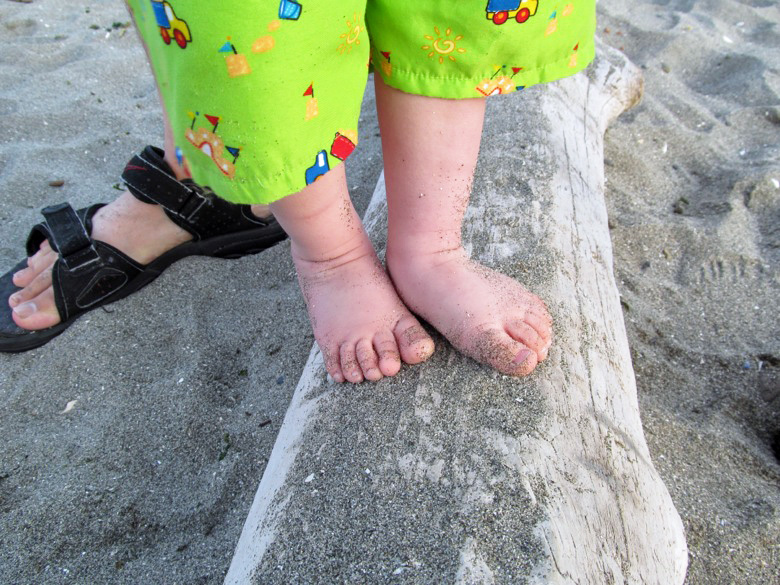 baby feet balancing on log on beach with mama in family camping