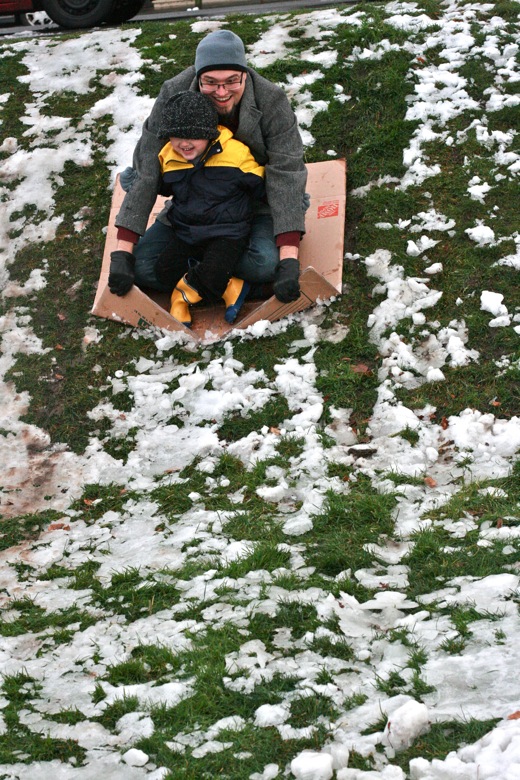 dad and boy sledding on cardboard box in winter outdoors in Seattle