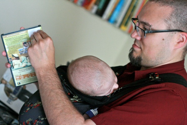 family business —  dad sam babywearing alrik anb newborn baby while working on dvd